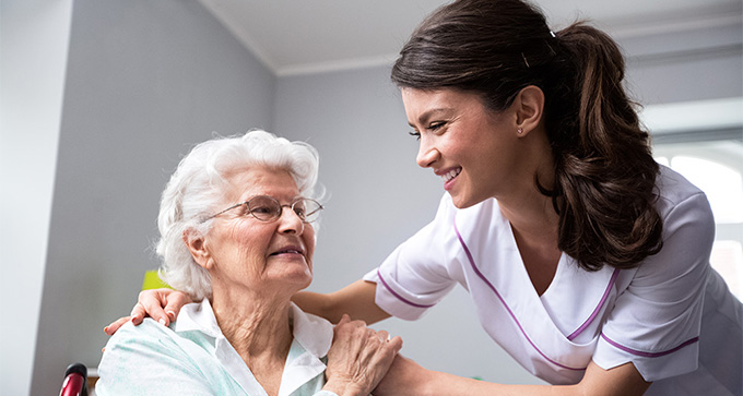 a carer in purple scrubs looking after an elderly lady in her home