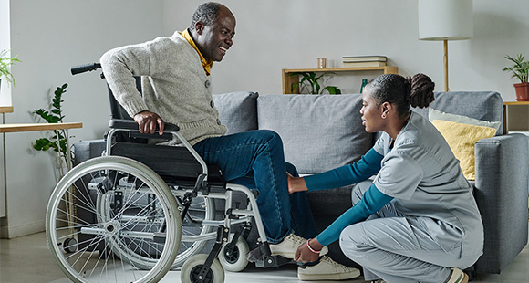 a carer holding a disabled man's foot to help him into a wheelchair