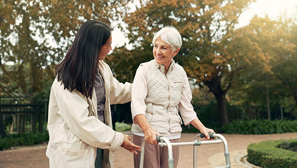 Carer helping senior woman with walker outside