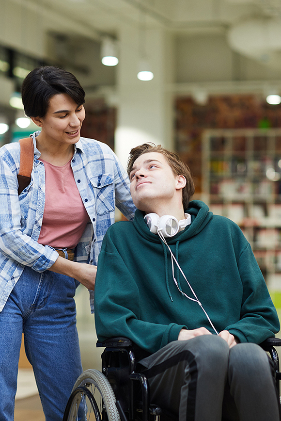 Young man in wheelchair being helped by personal carer